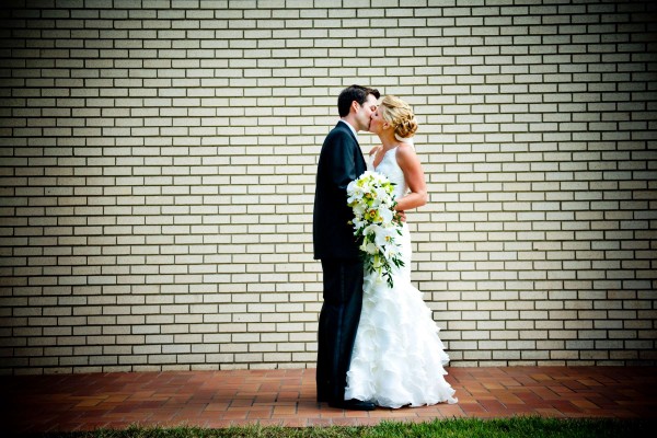 San Diego Wedding Photography: True Photography photographs bride and groom kissing in front of a brick wall after San Diego wedding ceremony 