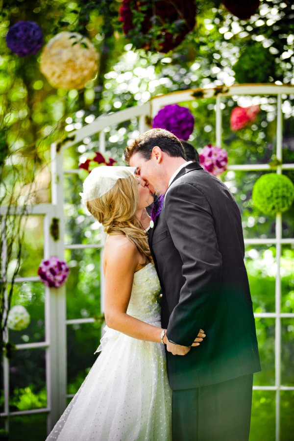 San Diego wedding photographer True Photography: bride and groom's first kiss during outdoor wedding with floral balls hanging from trees 