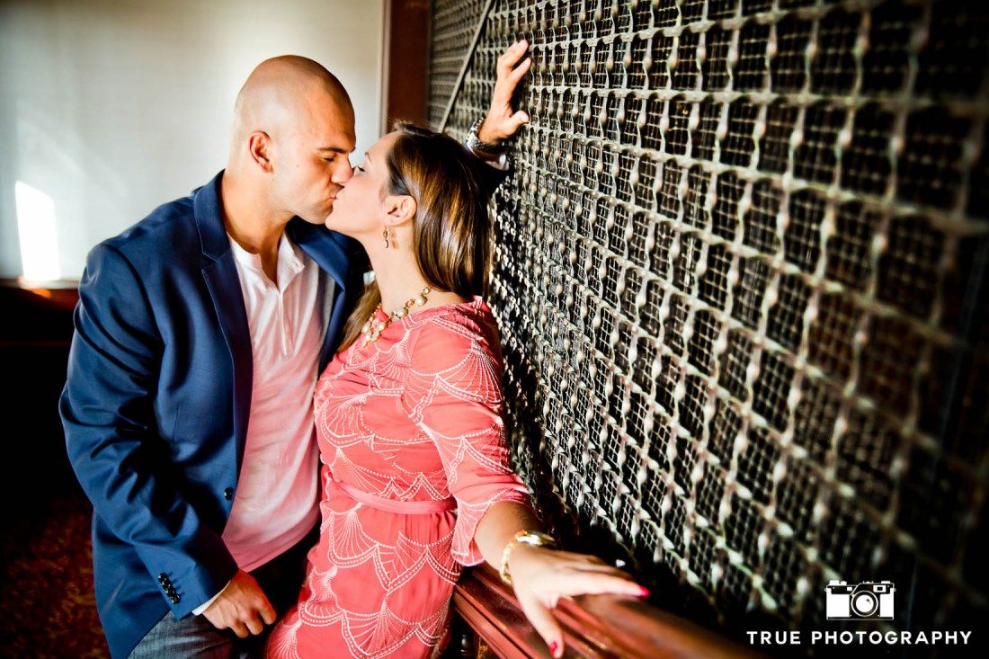 Engagement shoot of Del Mar Beach couple kissing against railing