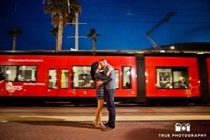 engaged couple kissing in front of trolley in Downtown San Diego