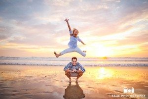 Engagement photo shoot of Mission Beach couple with the future bride jumping on beach