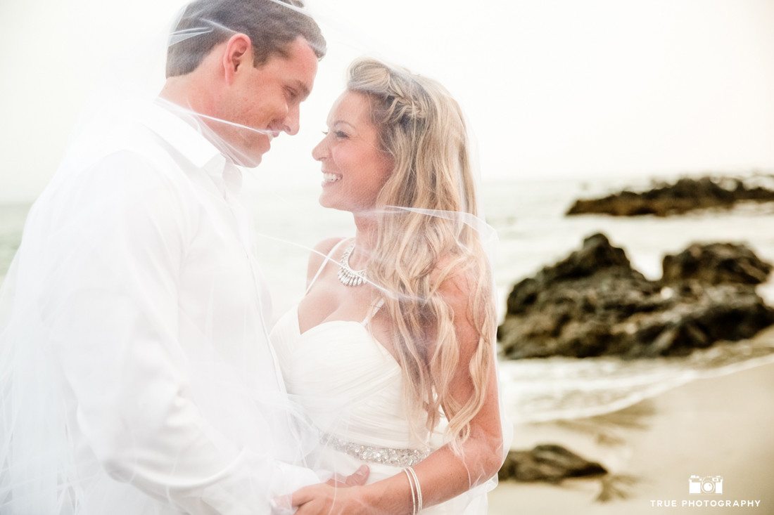Candid wedding moment under a veil on the rocky shores of Punta Mita