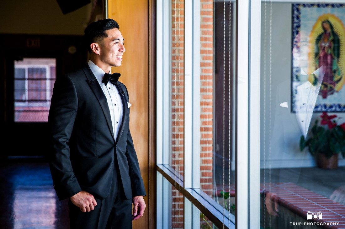 Groom in Black tuxedo with velvet bow-tie outside of church waiting for his bride.
