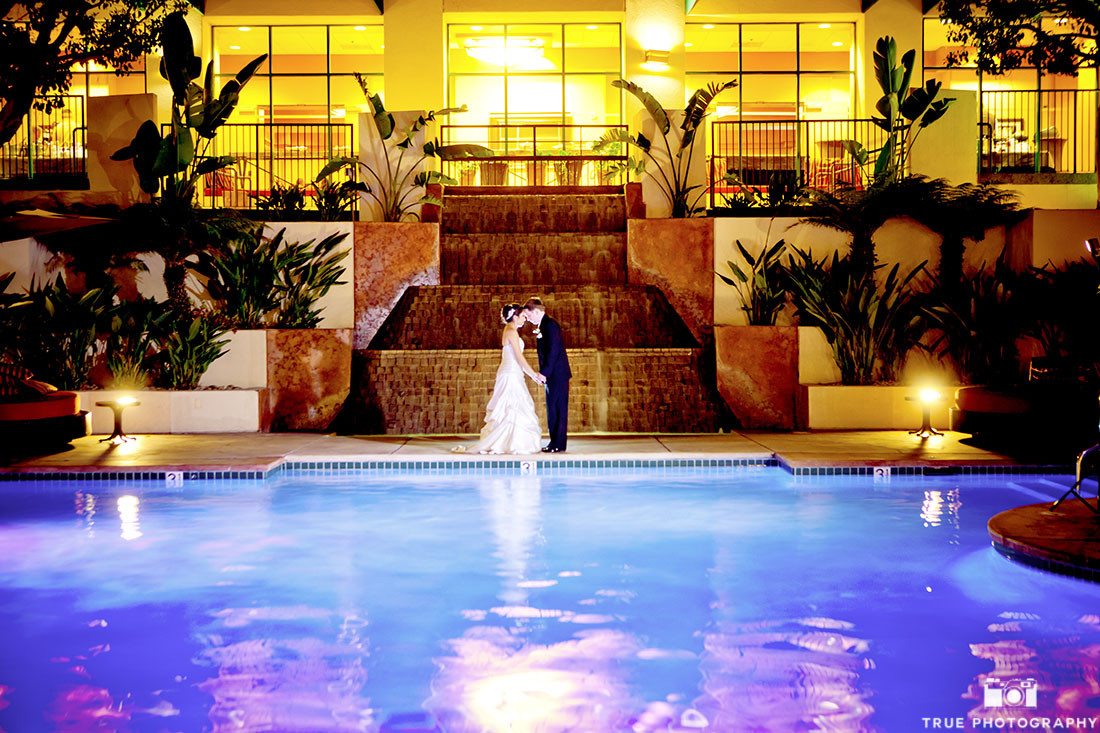 Romantic Evening Photo of bride and groom kissing by pool on their wedding day