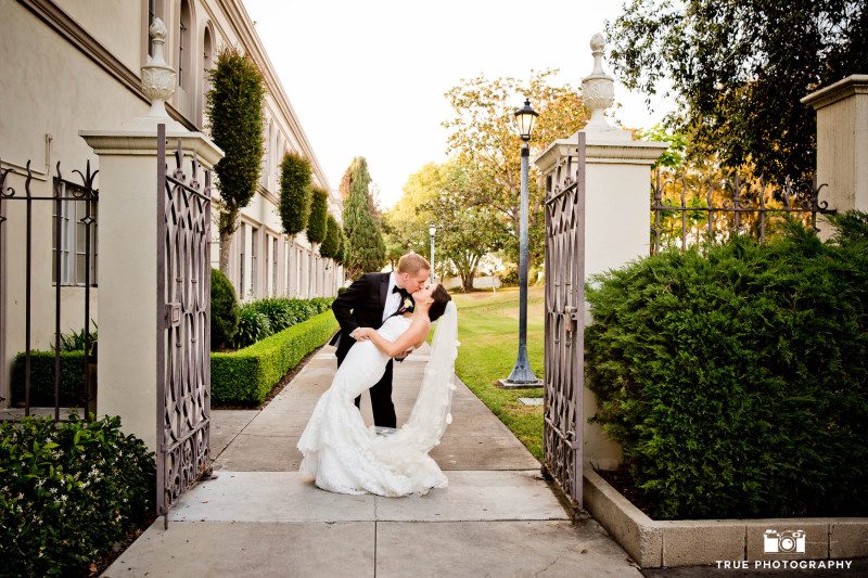 A groom tilts his new bride back for a fashionable kiss near the gates of Founders chapel.