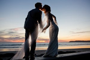 Bride and groom kissing during sunset while bride's veil is light up by off camera flash