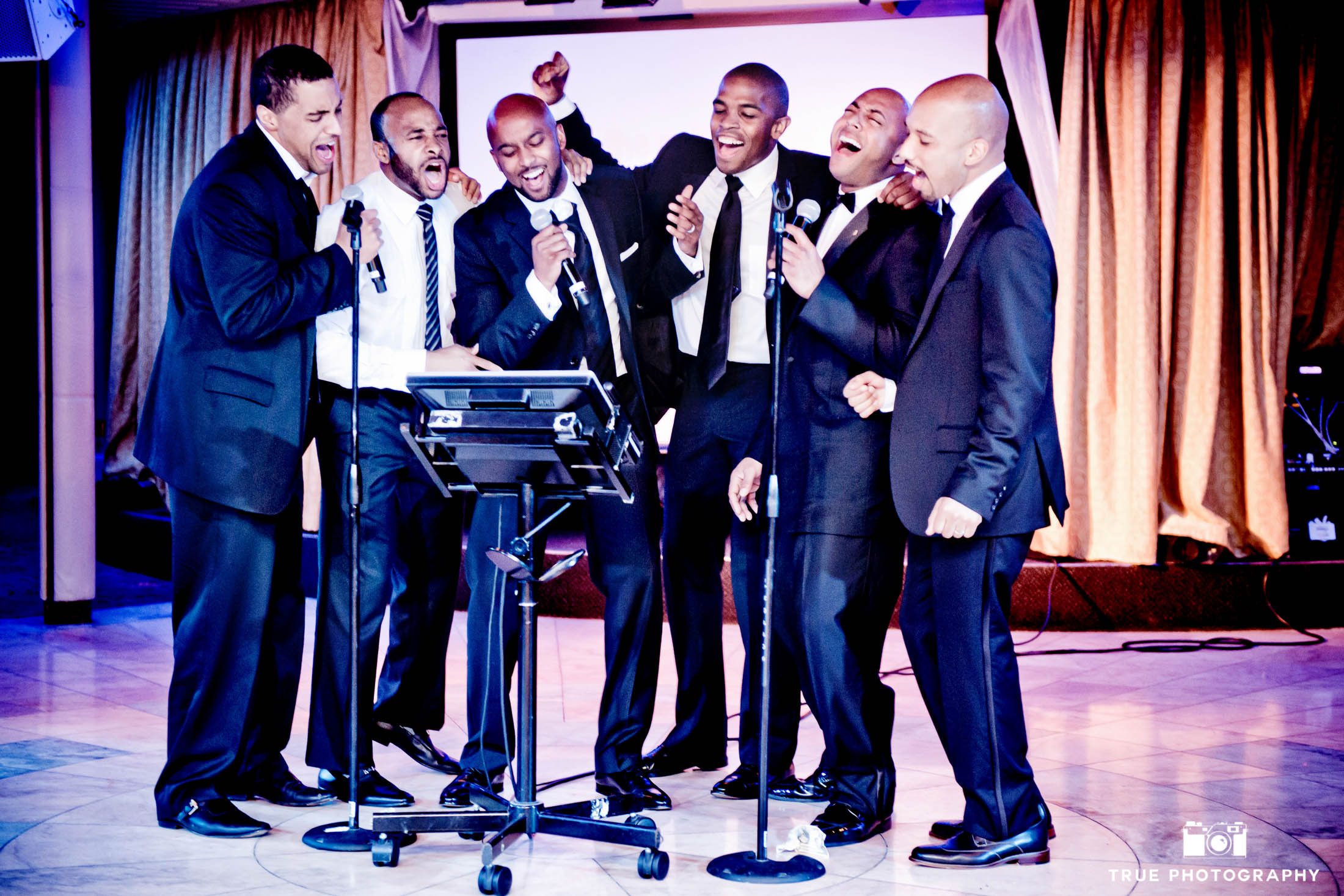Dapper men sing karaoke during a destination wedding.