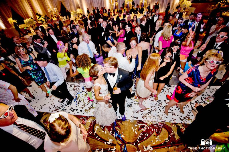Bride and Groom stand in crowd and kiss during wedding reception