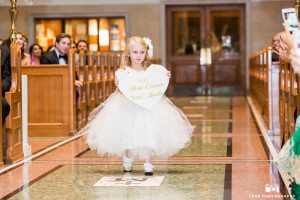 A flower girl in a tulle dress carries a heart down the aisle