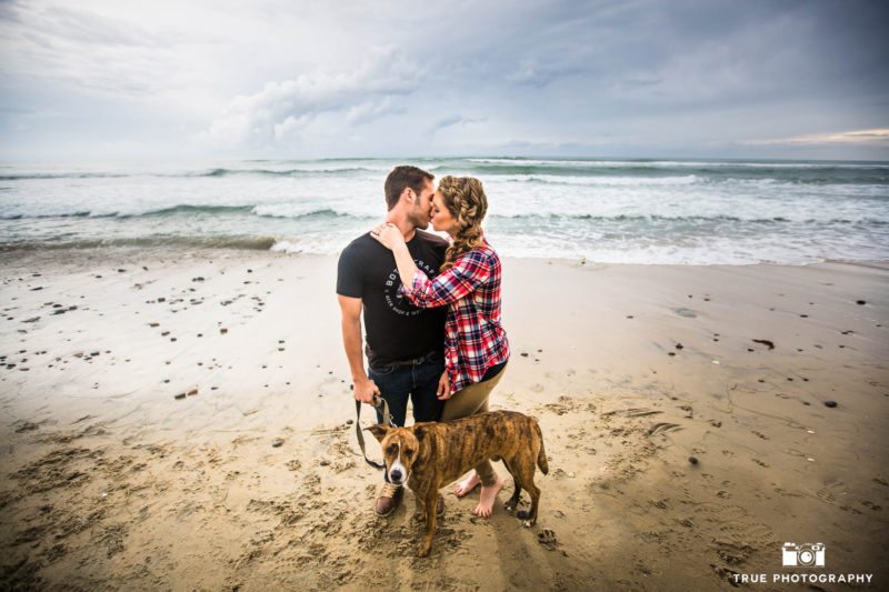 Couple kissing at beach with dog.