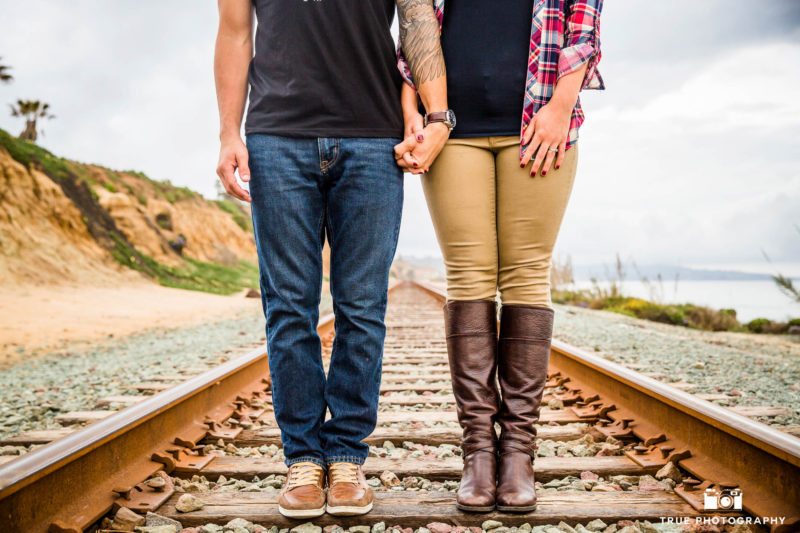 Couple standing on train tracks near beach.