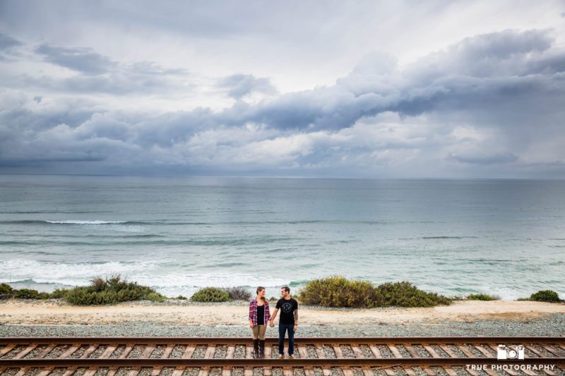 Couple holding hands on train tracks at San Diego beach engagement session.