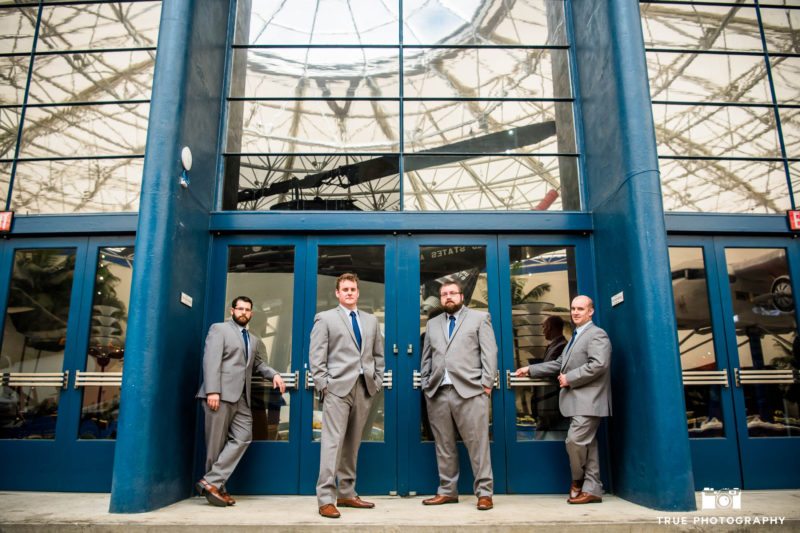 Groom and Groomsmen stand in front of blue doors at San Diego Air and Space Museum