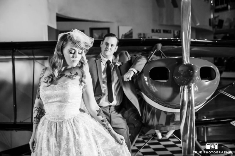 Black-and-white photo of bride and groom by airplane propellor