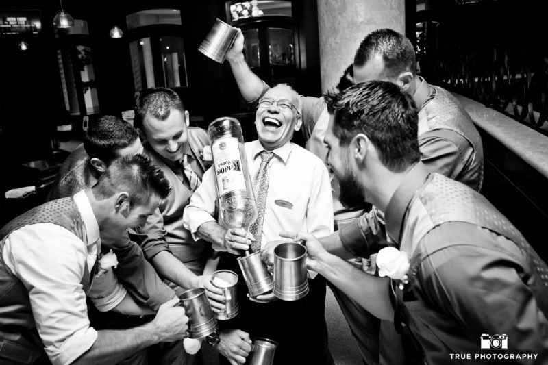 Funny, candid moment of Groomsmen with Dad drinking big bottle of liquor at wedding reception