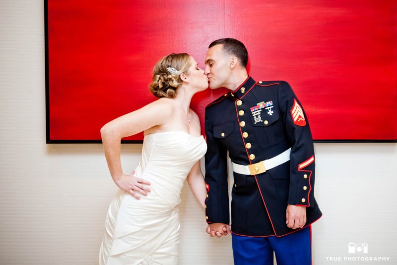 Military Groom and Bride hold hands and lean in for kiss by red painting