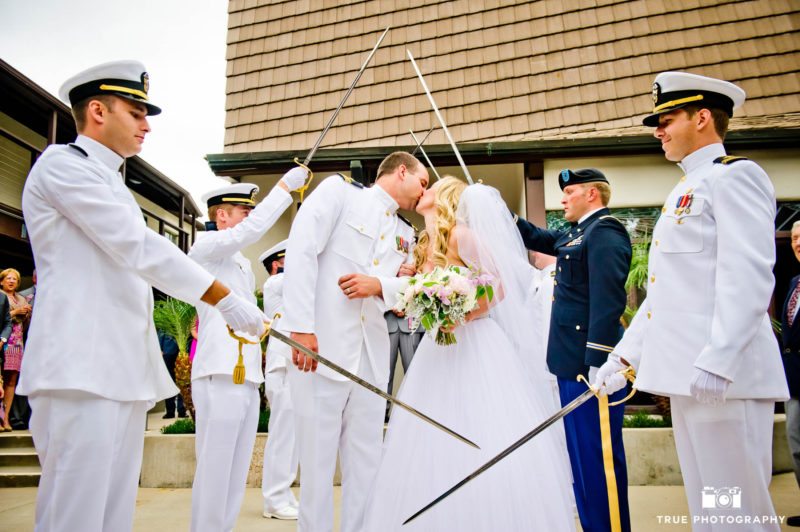Navy military groom and bride stop for kiss under arch of swords after wedding ceremony in Coronado, California