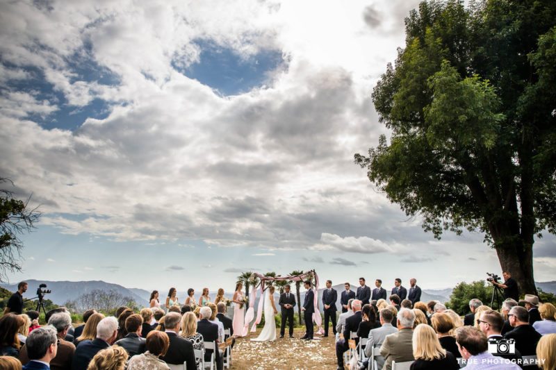 Wide-angle perspective of bride and groom tying the knot during rustic outdoor wedding ceremony