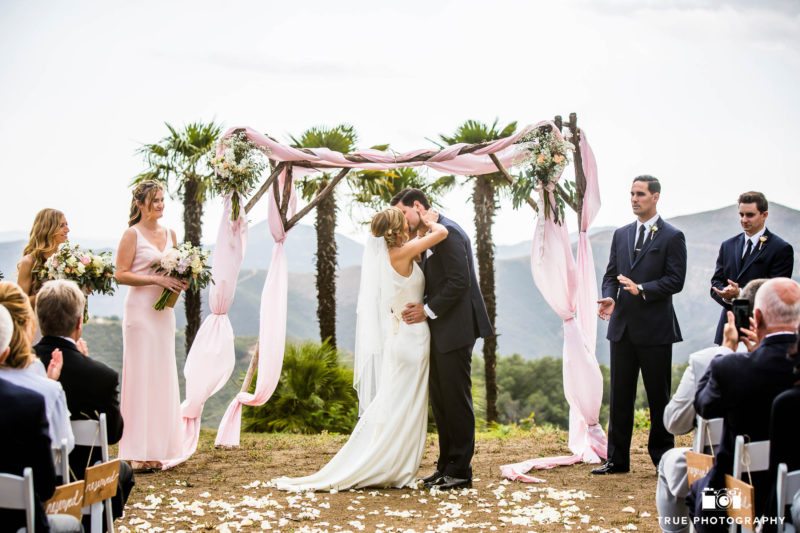 Groom dips Bride during First Kiss at outdoor wedding ceremony overlooking mountains