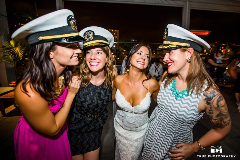 Bride poses with wedding guests as they laugh while wearing navy military hats