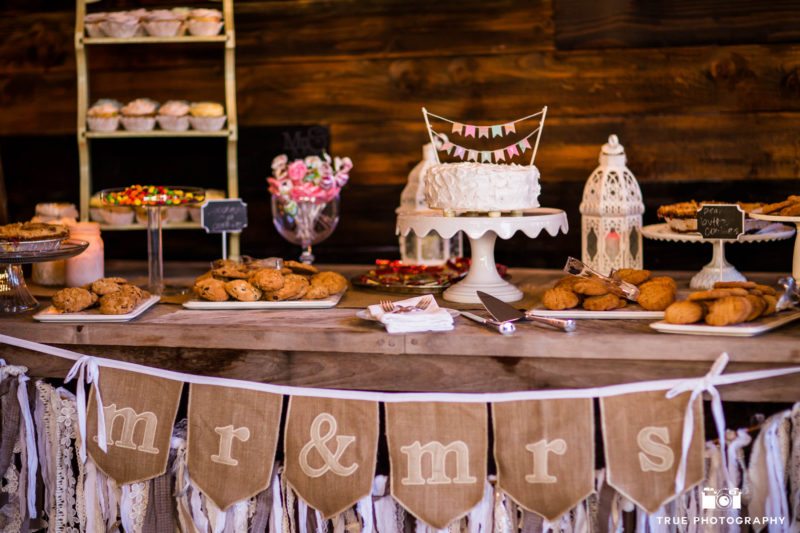 Dessert table with wedding cake, cookies and candy during rustic wedding reception