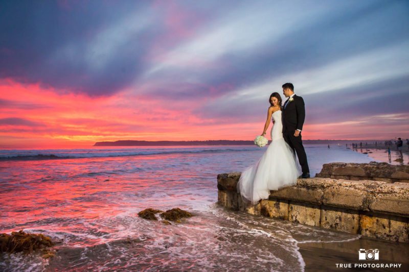Bride and Groom embrace on rock during Sunset