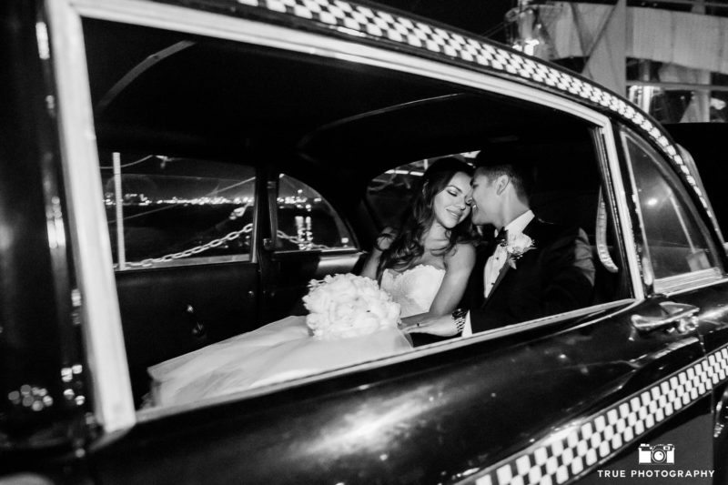 Black and white photo of bride and groom embracing in vintage limo