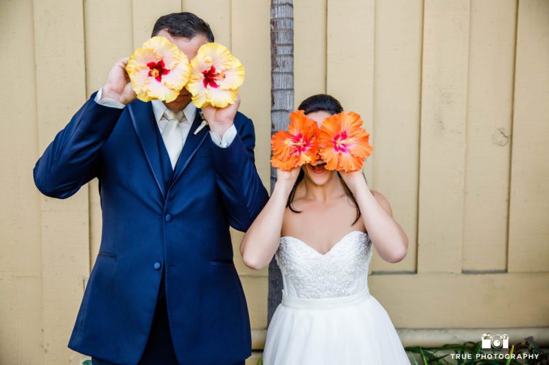 Funny Bride and Groom hold tropical flowers in front of faces