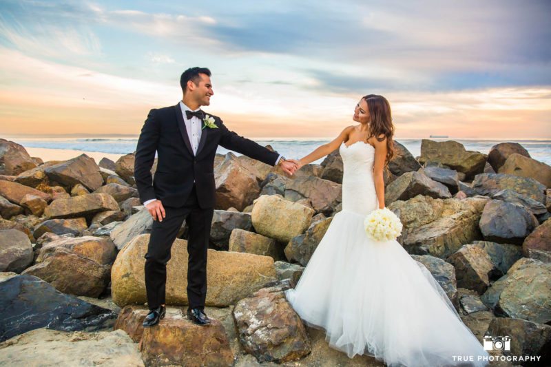 Bride and Groom hold hands on rocks at beach