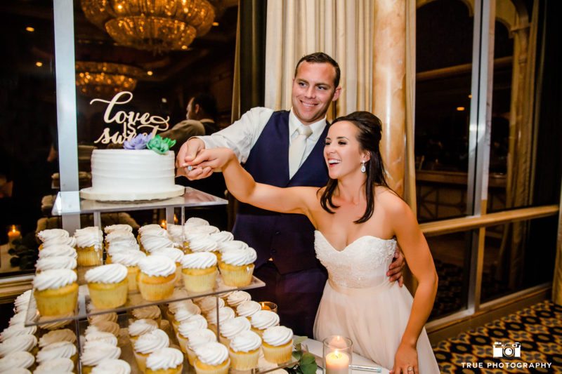 Bride and Groom hold hands and cut cake together during reception in Mission Ballroom at Bahia Resort