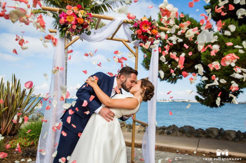 Bride and Groom Kiss under and arbor with flower petals