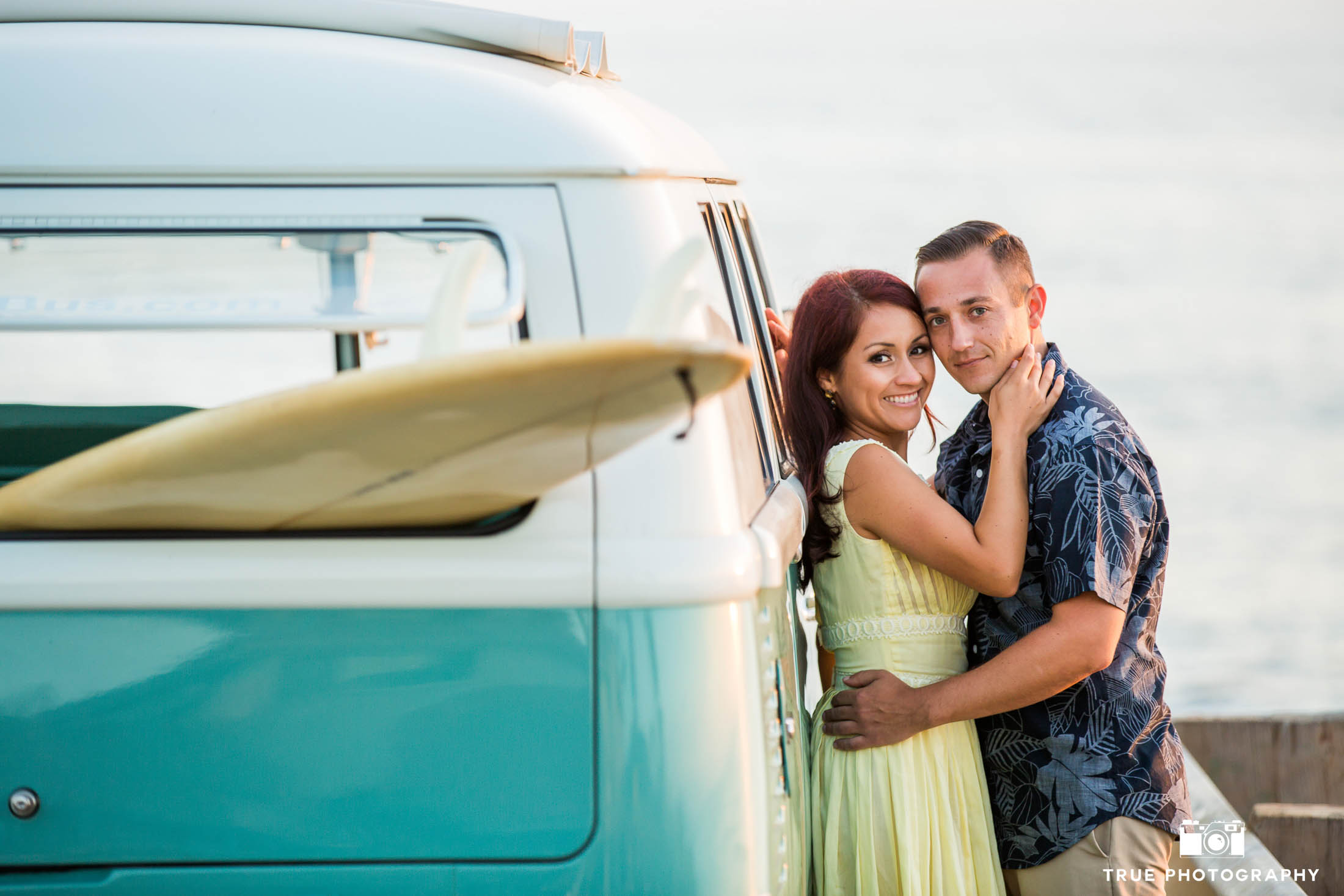Engaged couple embrace and lean against vintage Volkswagen bus during engagement session