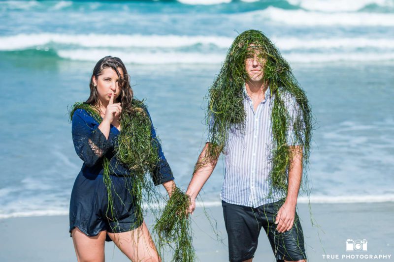 couple having fun while covered in seaweed during their engagement session