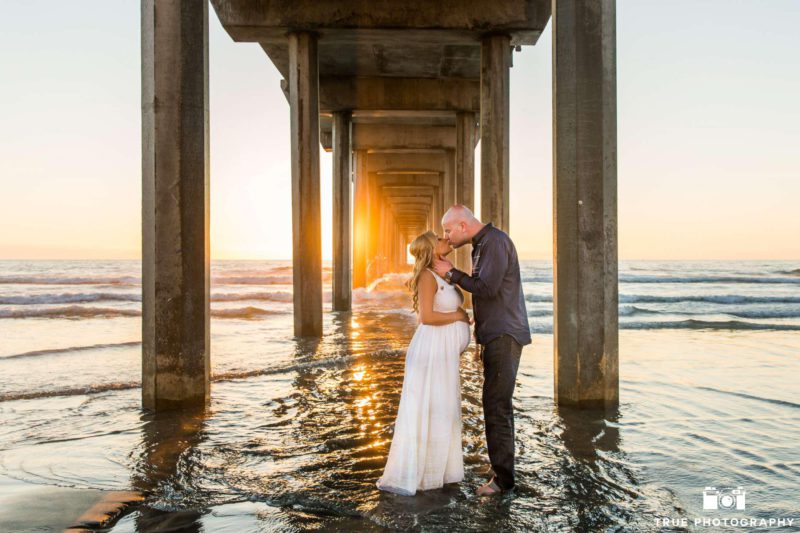 couple kissing under the pier during sunset at their maternity photo session