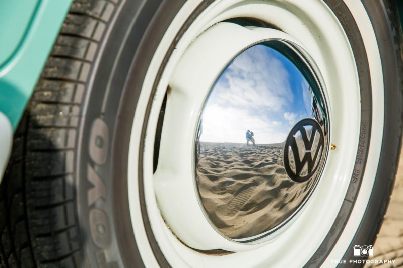 Reflection of engaged couple kissing in metal hubcap of volkswagen bus