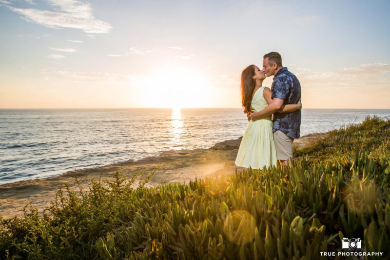 Engaged couple embrace and kiss one another during sunset at Sunset Cliffs