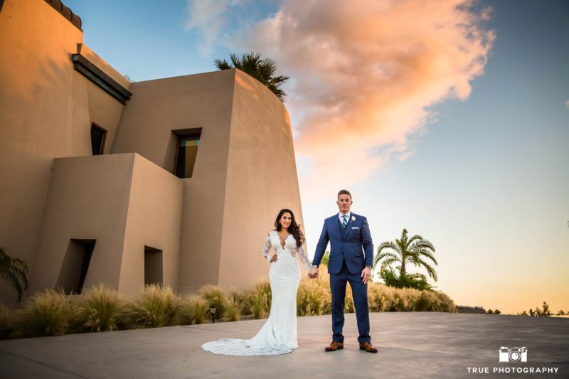 Bride and Groom stand in front of colorful sunset on wedding day