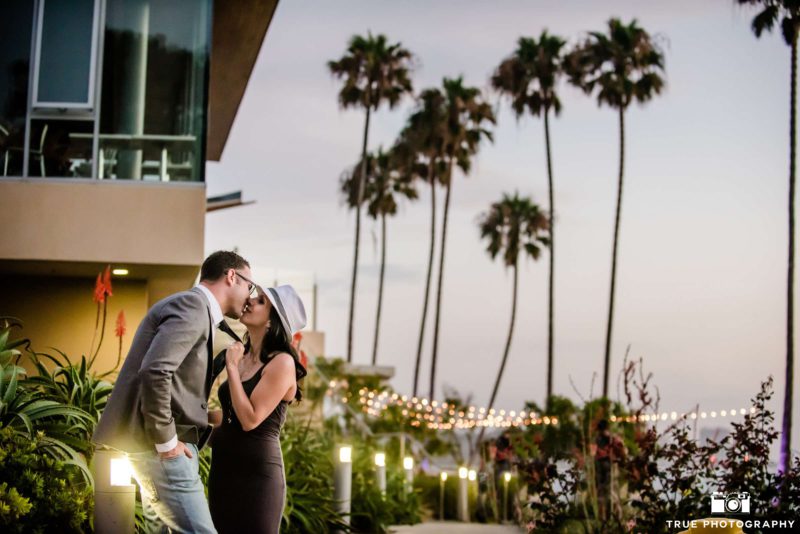 Couple kissing amidst palm trees.