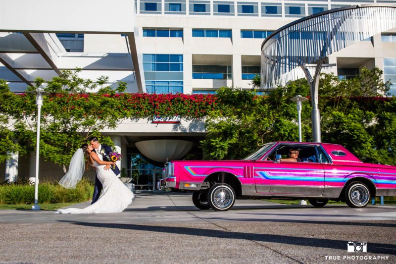 Bride and Groom kiss next to pink low rider car
