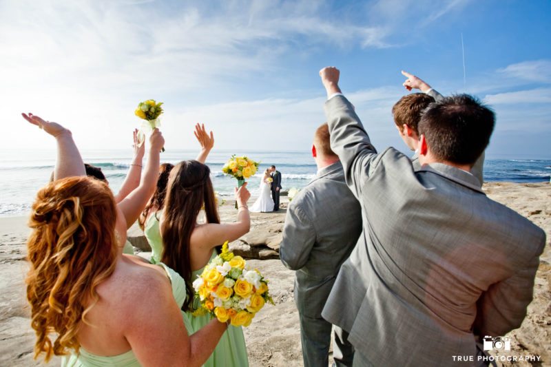 bridal party cheer on wedding couple as they kiss on beach
