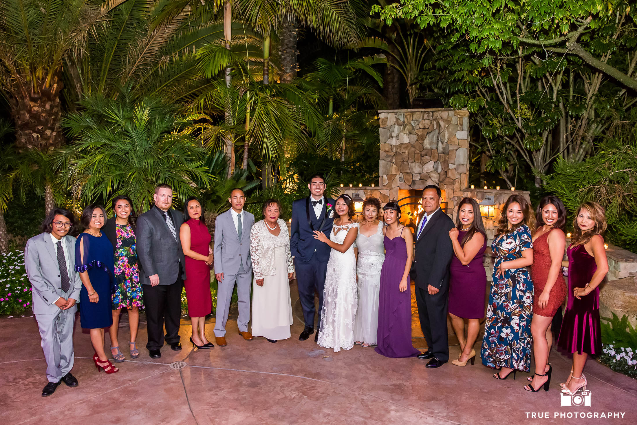 A wedding group takes a photo in front of a fireplace.
