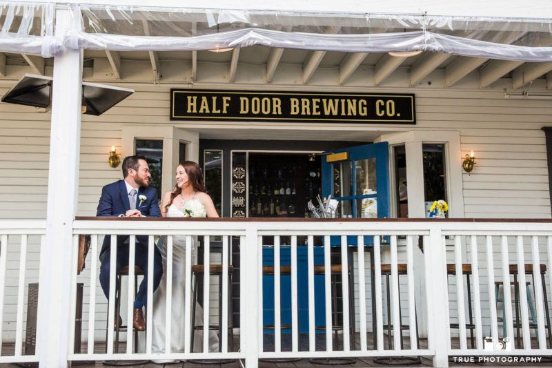 Bride and groom sit laughing on balcony at bar