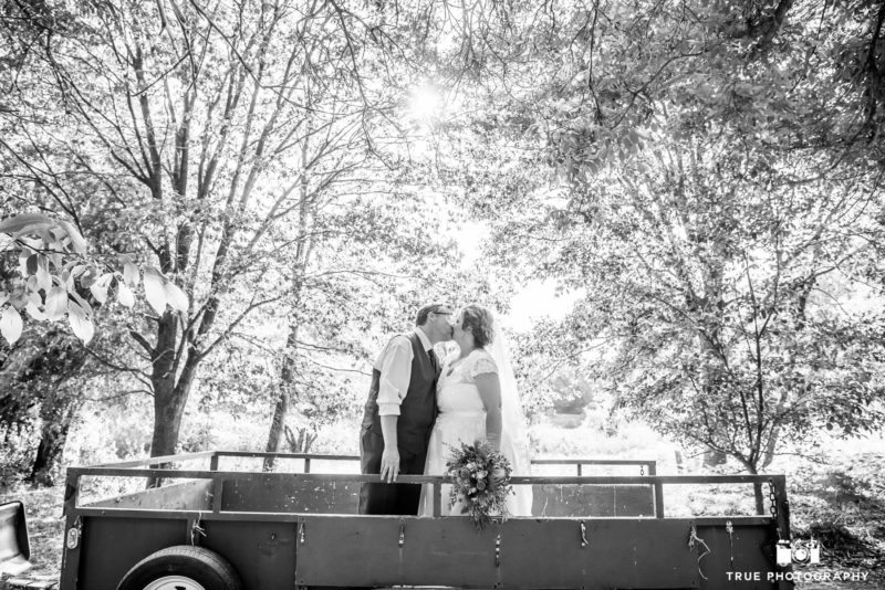 Bride and Groom kissing on flatbed truck after their rustic wedding ceremony