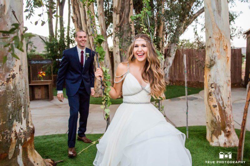Groom pushes happy bride on wooden swing