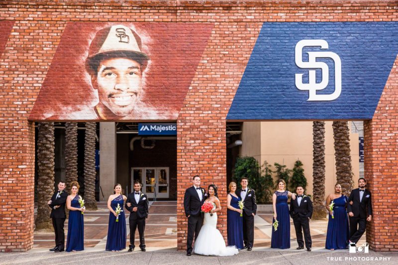 Wedding couple pose with bridal party under brick opening at petco park
