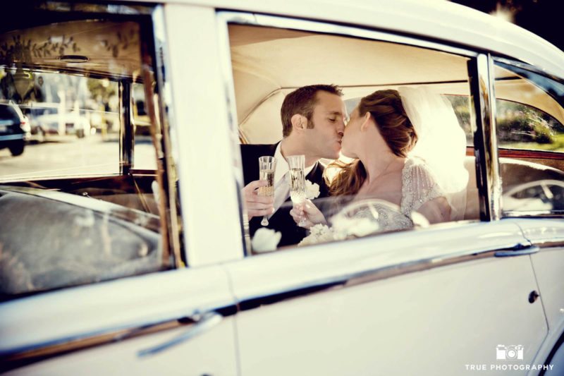 Bride and groom kiss in a white car.