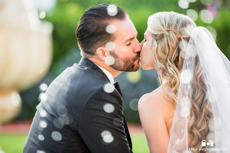 Creative portrait of wedding couple kissing by fountain