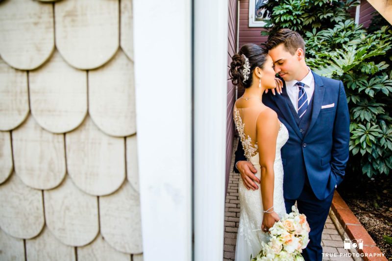 Groom and Bride embrace by wall at the Beverly Mansion