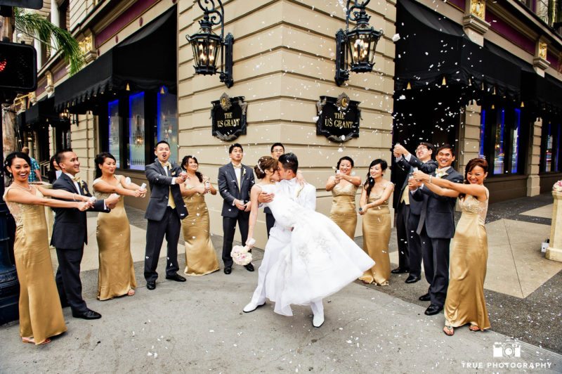 Bridal party throwing confetti while bride and groom kiss